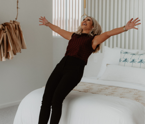 Image of a happy home owner falling onto white bed after buying from a buyers agent